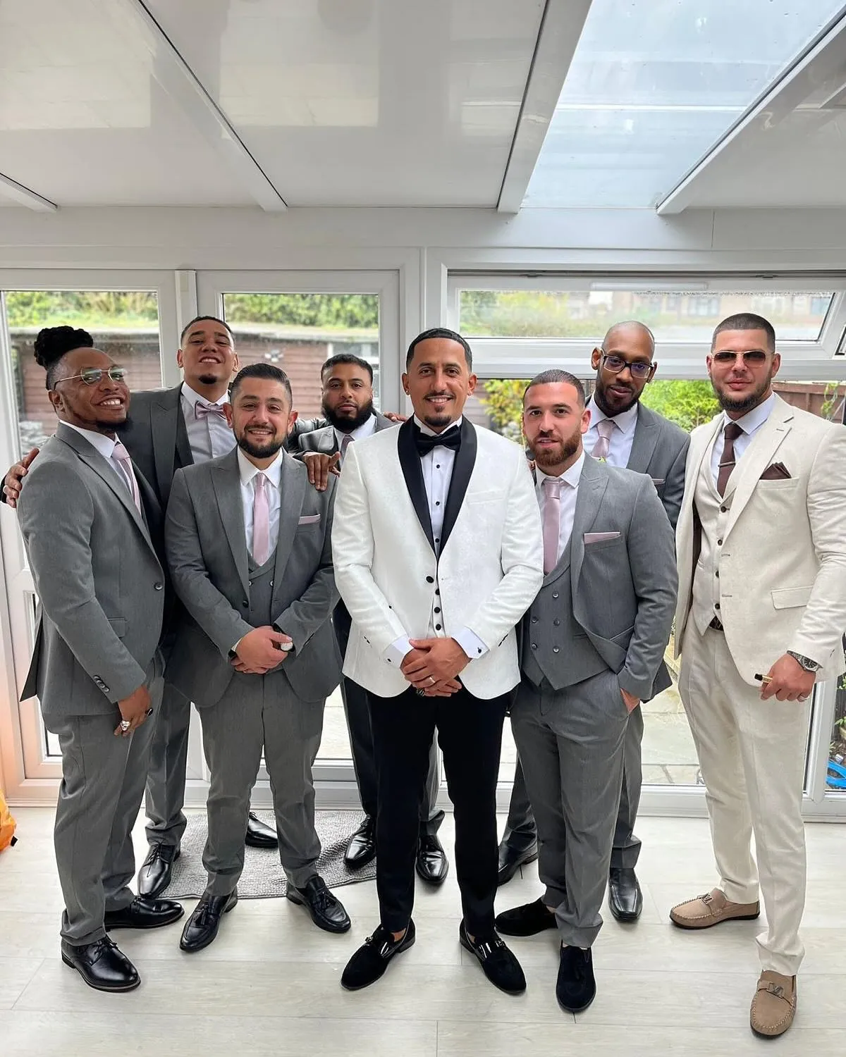 Groom in a white tuxedo with his groomsmen in grey suits